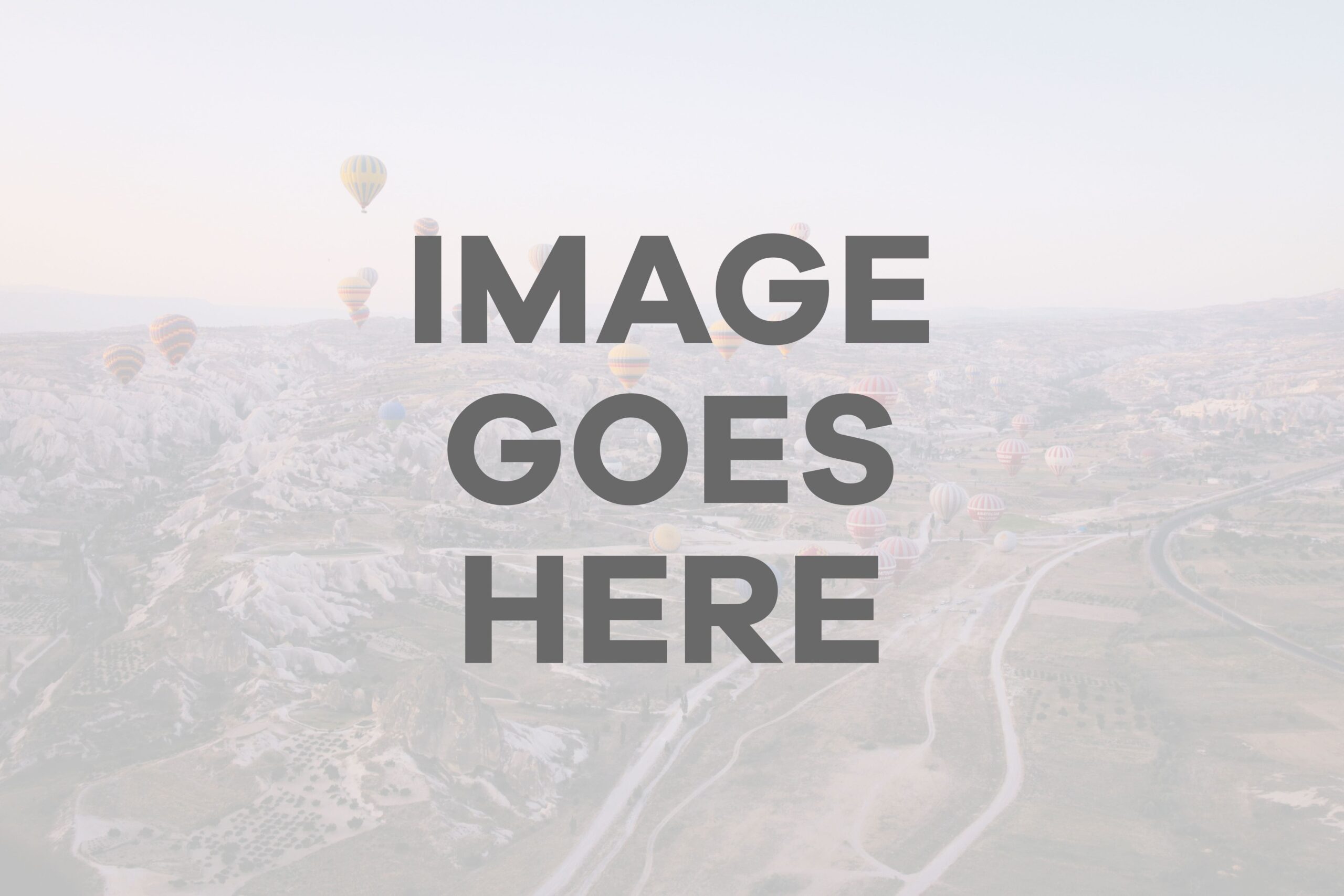 Aerial view of landscape with hot air balloons floating above fields and roads at sunrise.