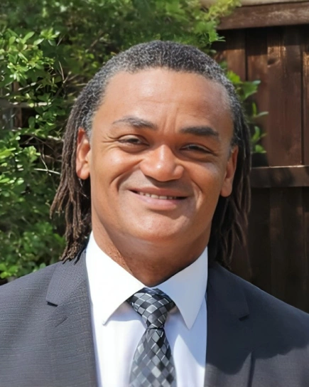 Professional headshot of man in business suit against outdoor foliage background for dental practice.