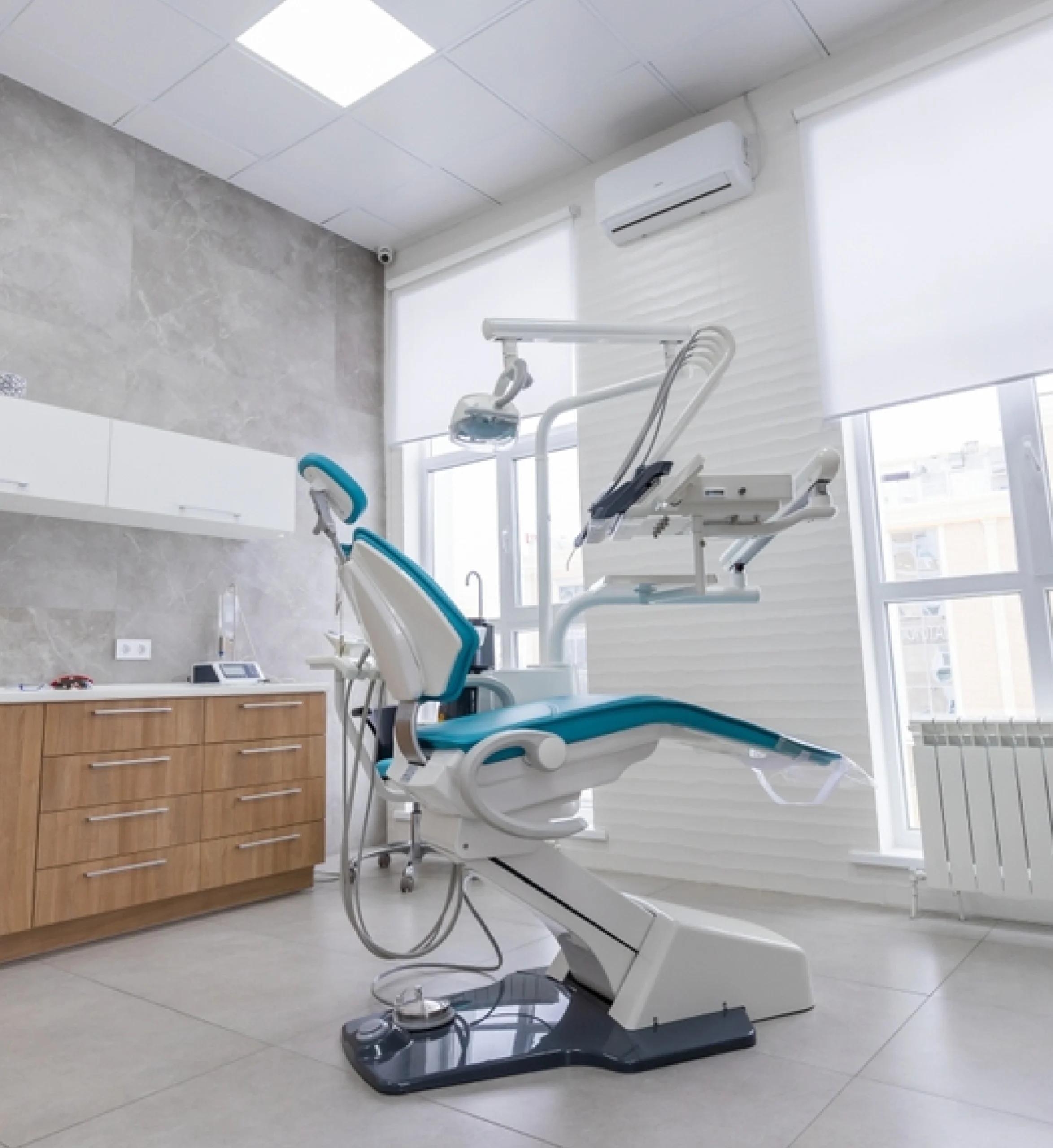 Modern dental operatory with blue treatment chair in bright, clean clinical setting with equipment.