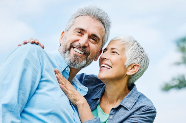 Happy senior couple smiling outdoors in casual clothing during daytime.