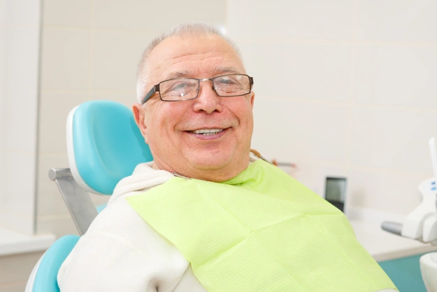 Smiling patient in dental chair wearing bib at modern dental office